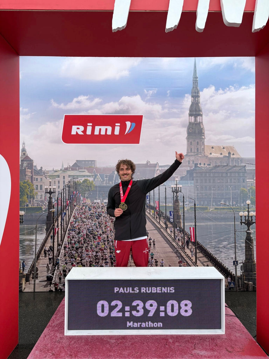 Pauls Rubenis uz Rimi Rīgas maratona goda pjedestāla ar medaļu; tablo rāda 02:39:08